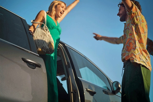 Woman exiting a car and about to hug a male friend