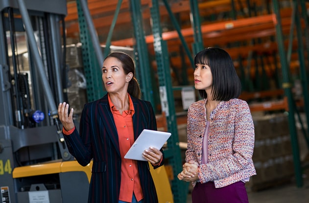 Two woman discussing business while observing an event in a factory.