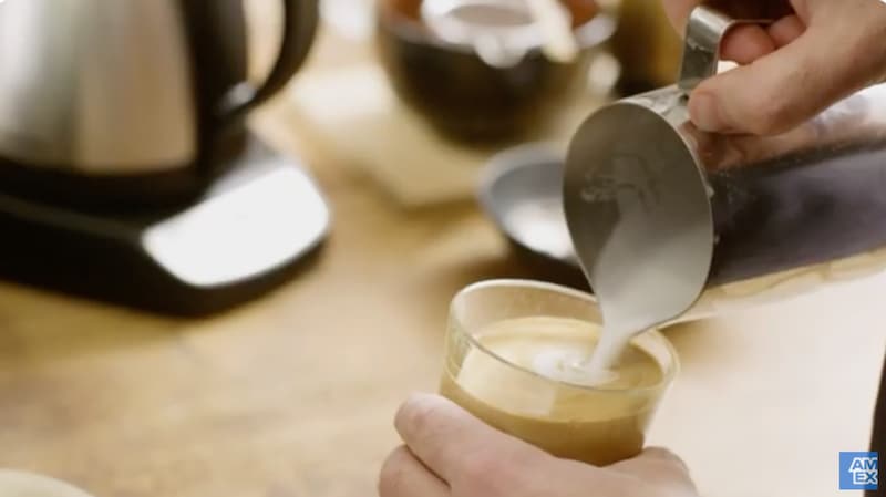 Coffee store barista pouring latte into glass