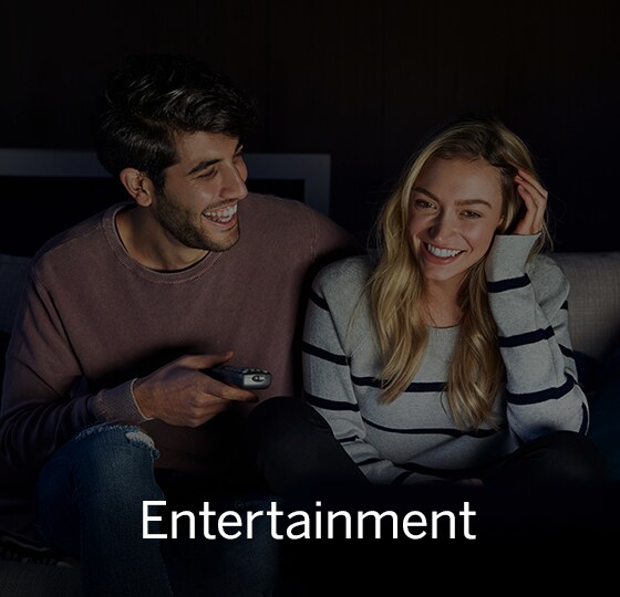 Male and female holding television remote control in dark lit room. Text over image - Entertainment.