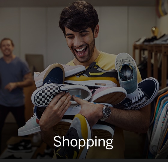 Male laughing with overflowing arms full of sneakers. Text over image - Shopping.