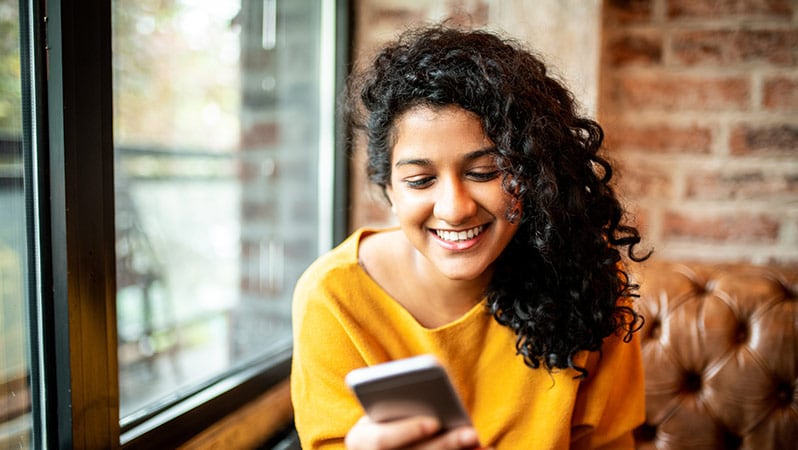 A lady smiling looking at her smartphone screen.