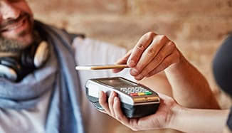 A man making payment using his smartphone by holding it up to a contactless reader.