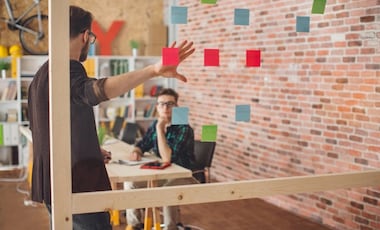 Two people talking and looking at post-it notes on a transparent board while brainstorming