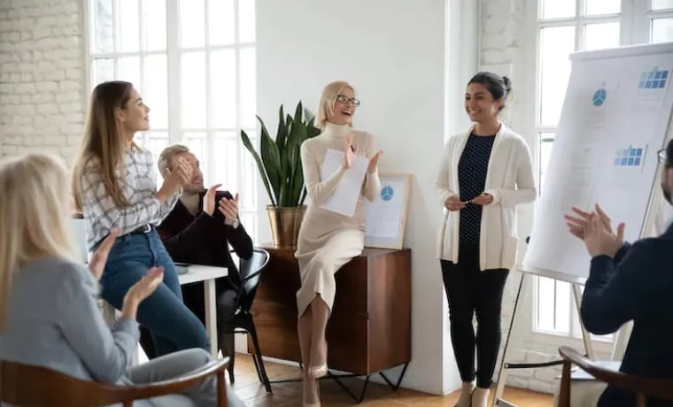 Coworkers standing in circle and clapping for someone's presentation