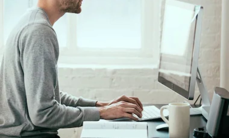 Person sitting at desk and typing on keyboard while looking at desktop device