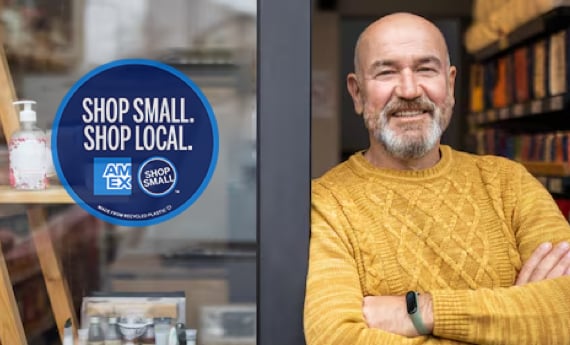 Business owner standing next to storefront with Shop Small with Amex sign in window