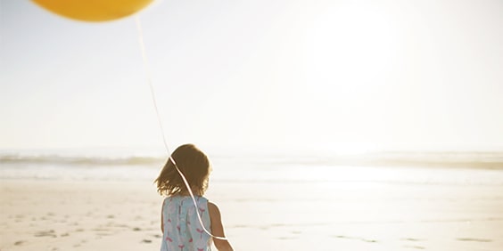 Child walking on beach holding a yellow balloon.