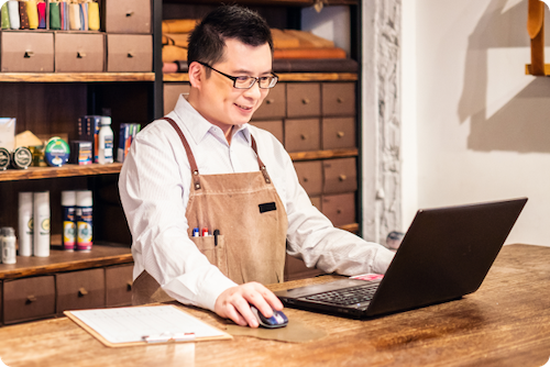 Small business owner standing at counter and looking at laptop