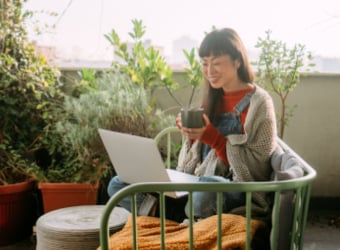 Woman sitting on couch with coffee mug while looking at laptop