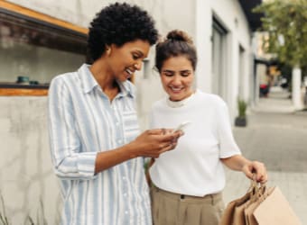 Two woman on sidewalk smiling and looking at phone