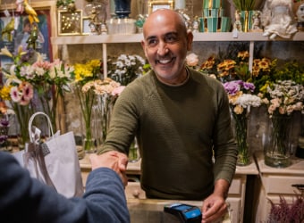 Man behind counter in flower shop shaking the hand of a customer