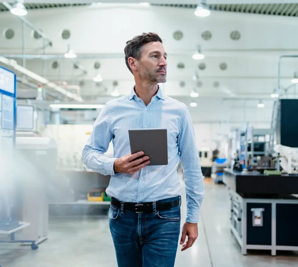 Mann in Hemd läuft mit einem Tablet durch eine moderne Produktionshalle.