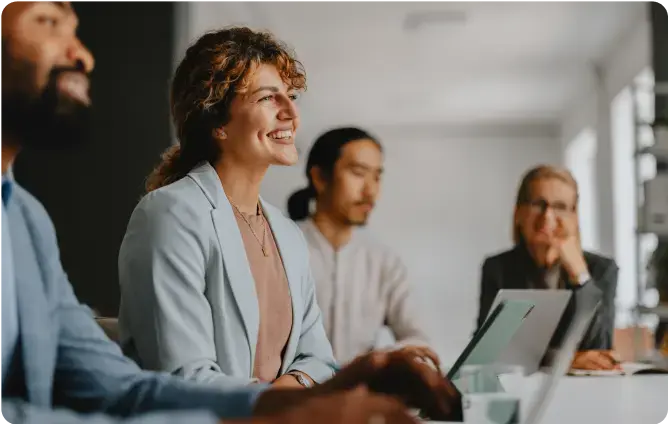 Vier Personen sitzen in einem Meeting und lächeln, während sie konzentriert zuhören.
