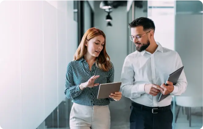Zwei Kolleg:innen stehen im Büroflur und besprechen Inhalte auf einem Tablet.