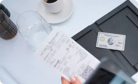 Nahaufnahme einer Restaurantrechnung neben einem American Express Business Platinum Card auf einem Tisch mit Getränken.