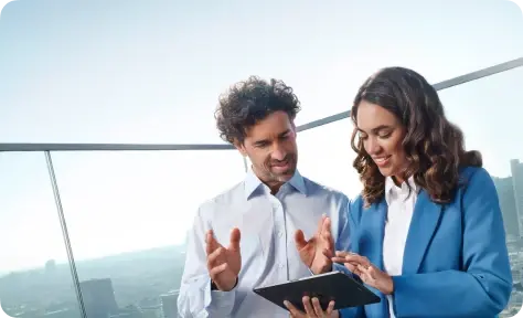 Geschäftspartner im Gespräch, während sie gemeinsam auf ein Tablet schauen, vor einem Stadtpanorama.