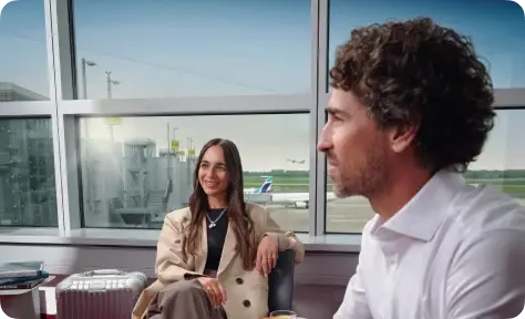 Zwei Geschäftsreisende entspannen in einer Flughafenlounge mit Blick auf das Rollfeld.