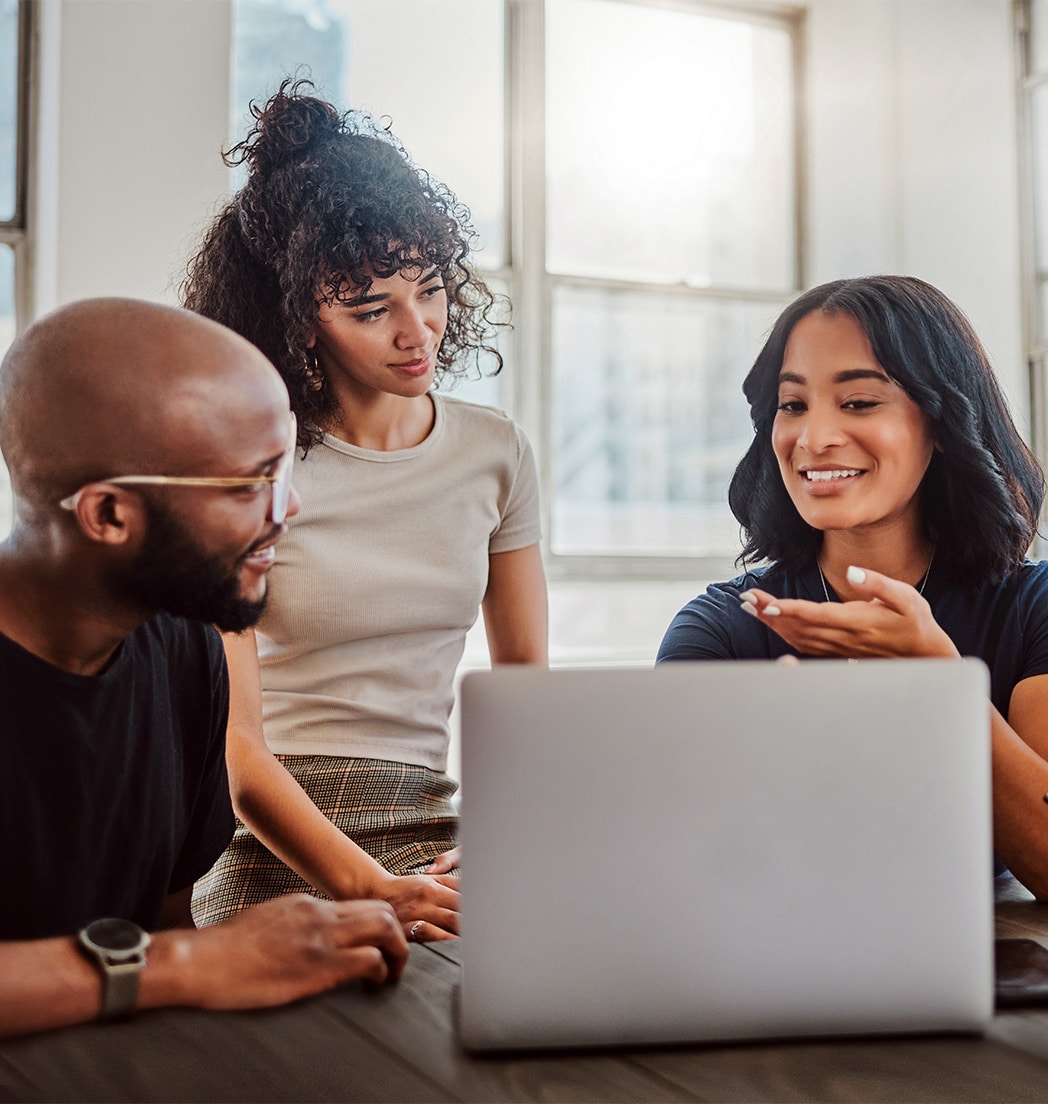 Drei Menschen, die vor einem Laptop sitzen und miteinander sprechen