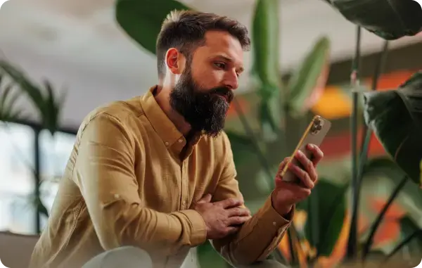 Mann mit Bart sitzt in einem Café und schaut auf sein Smartphone