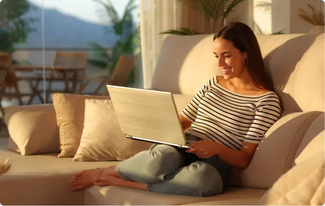 Frau sitzt entspannt auf einem Sofa und arbeitet mit einem Laptop