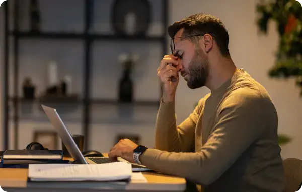 Mann sitzt abends am Laptop und hält sich nachdenklich die Stirn