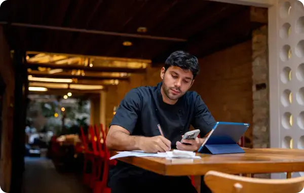 Mann sitzt im Restaurant und schreibt mit Smartphone und Tablet Notizen