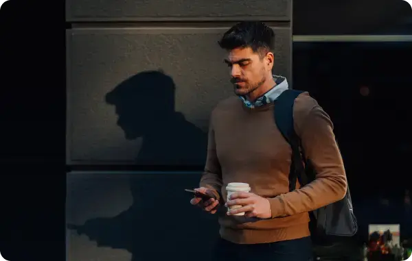 Mann mit Rucksack geht an einer Wand entlang und schaut auf sein Smartphone