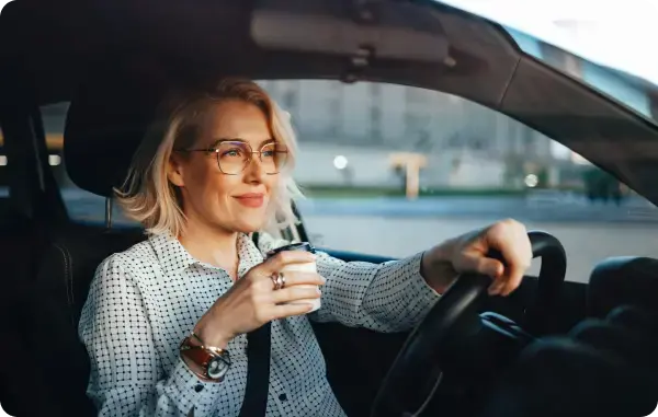 Frau sitzt am Steuer eines Autos und hält einen Kaffeebecher