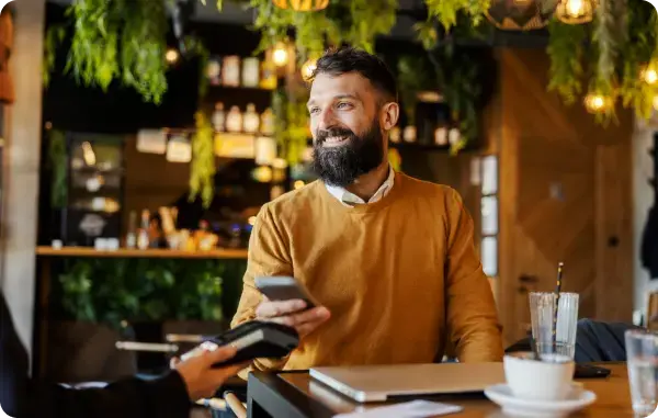 Mann bezahlt in einem Café kontaktlos mit seinem Smartphone