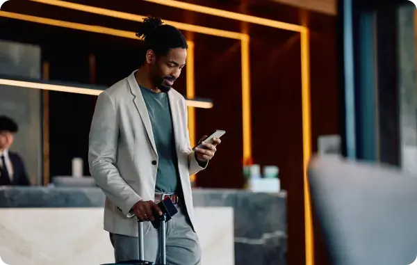 Geschäftsmann mit Reisekoffer nutzt sein Smartphone in einer Hotellobby