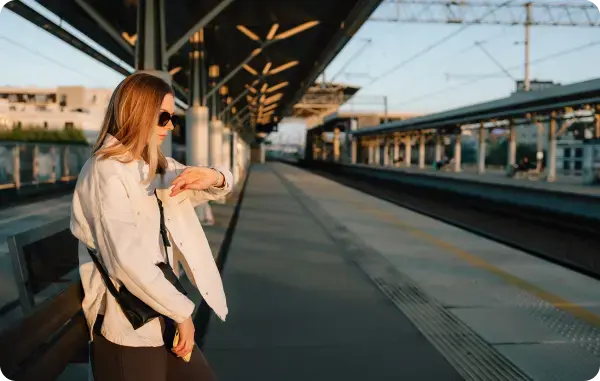 Frau wartet auf einem Bahnsteig und schaut auf ihre Uhr