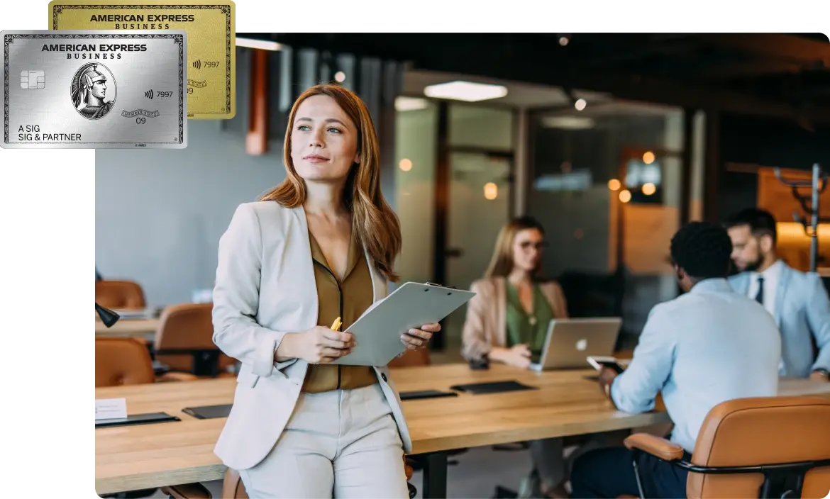 Frau im Business-Outfit mit Klemmbrett steht selbstbewusst in einem modernen Konferenzraum, im Hintergrund arbeiten Kollegen an Laptops.