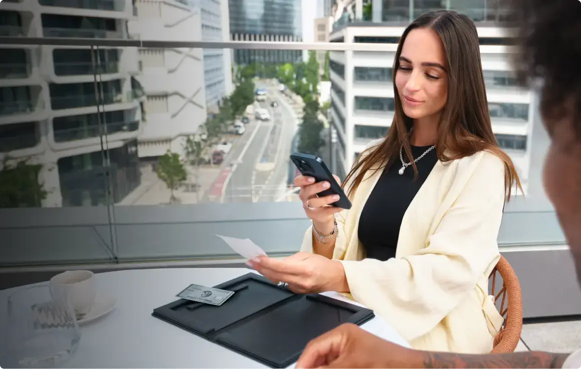 Junge Unternehmerin scannt eine Quittung mit ihrem Smartphone für die Buchhaltung über GetMyInvoices nach dem Geschäftsessen. Daneben liegt eine American Express Business Platinum Card aus Metall.