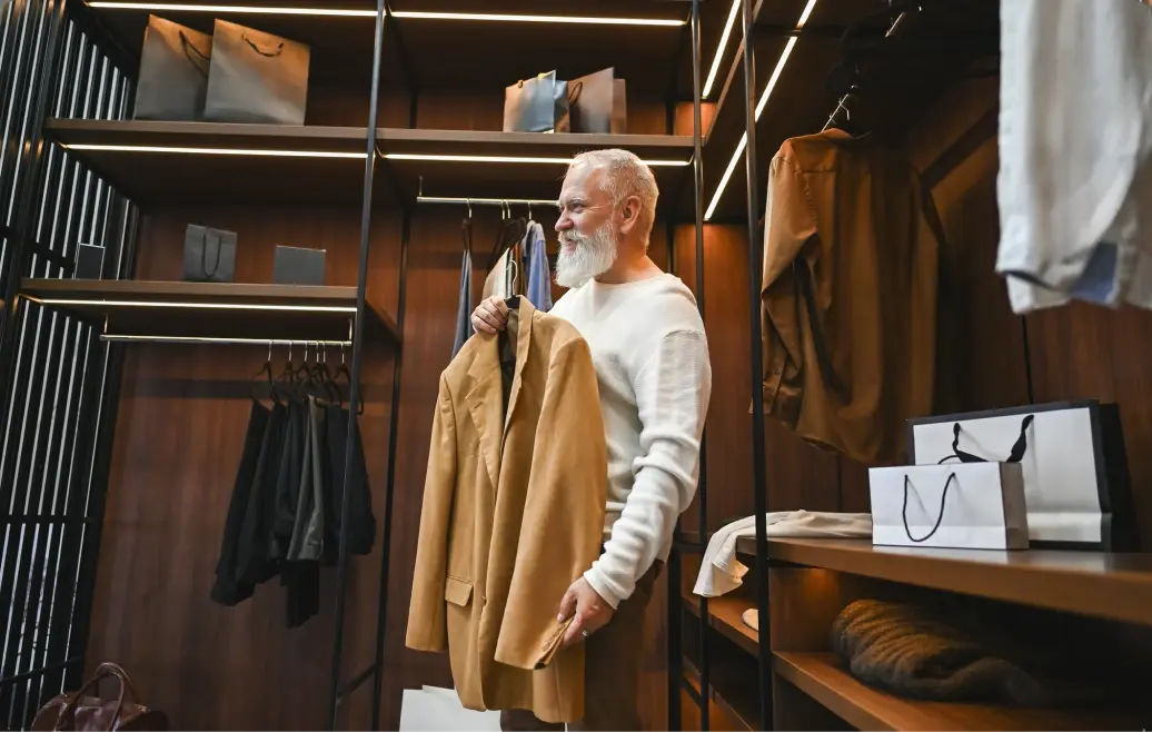 Mann steht in einer edlen Boutique und hält ein hellbraunes Sakko in der Hand.