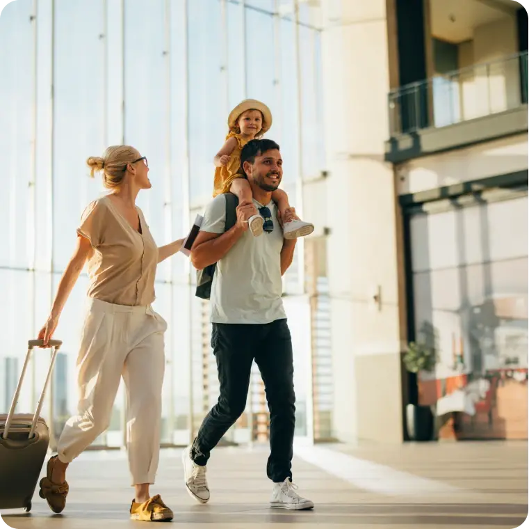Eltern mit Kind und Gepäck laufen durch eine helle Flughafenhalle.