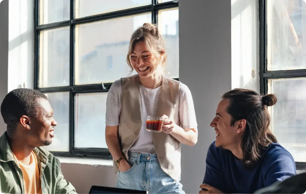Drei Kolleg:innen lächeln in einem modernen Büro, während miteinander sprechen.