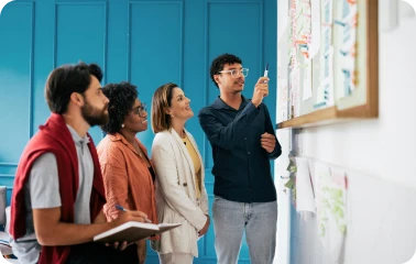 Vier Personen stehen vor einer blauen Wand und besprechen gemeinsam ein Architekturmodell.