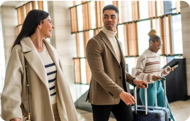 Zwei Frauen und ein Mann unterhalten sich im Flughafen, alle haben einen Rollkoffer.
