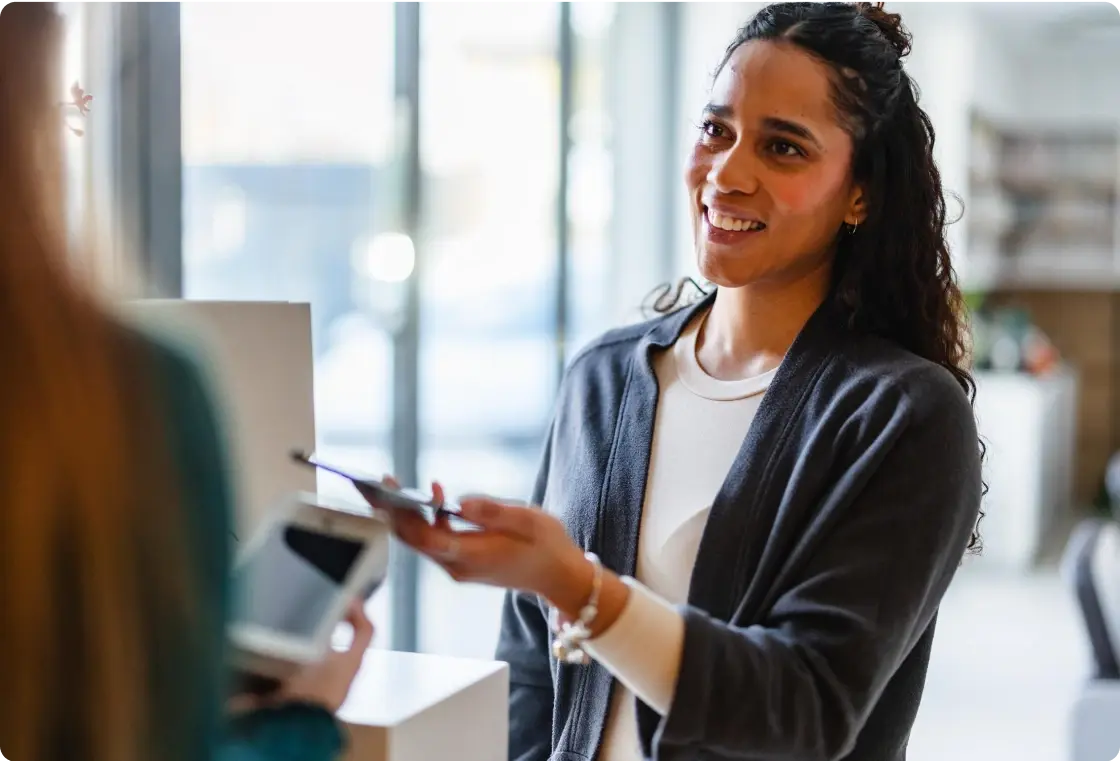 Frau bezahlt mit ihrem Smartphone kontaktlos an einem Kassenterminal und lächelt freundlich.