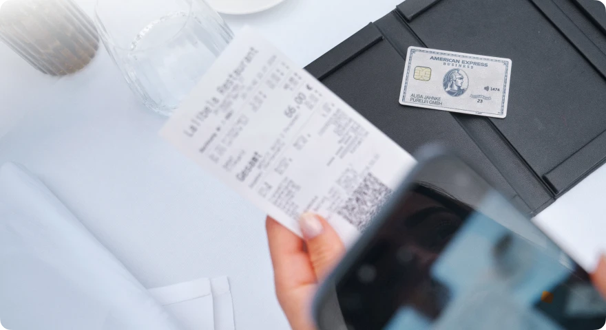 Nahaufnahme einer Restaurantrechnung neben einem American Express Business Platinum Card auf einem Tisch mit Getränken.