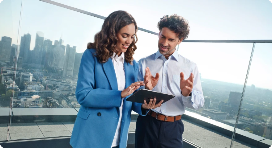 Geschäftspartner im Gespräch auf einer Dachterrasse mit Blick auf die Skyline, während sie gemeinsam ein Tablet nutzen.