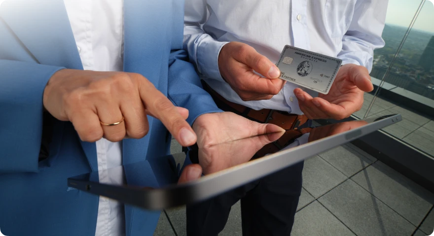 Zwei Personen nutzen ein Tablet, während einer eine American Express Business Platinum Card in der Hand hält.