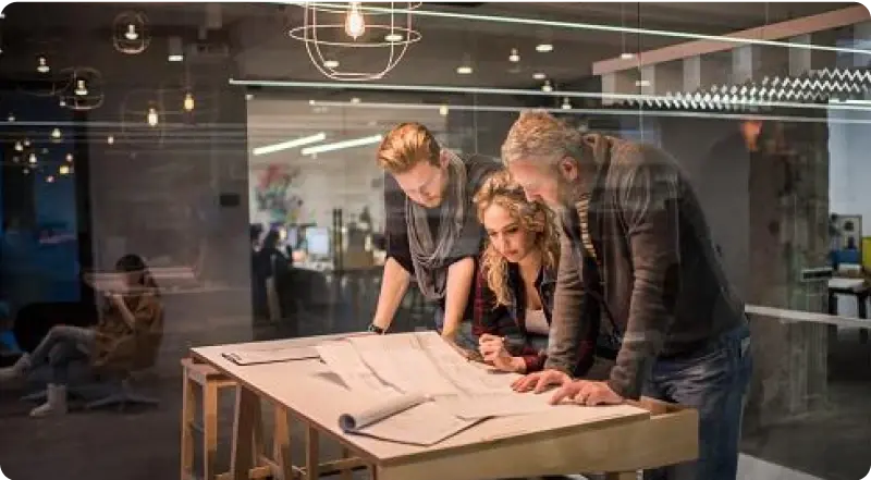 Drei Unternehmer:innen planen gemeinsam an Bauplänen – Investitionen mit American Express Business Card erleichtern.