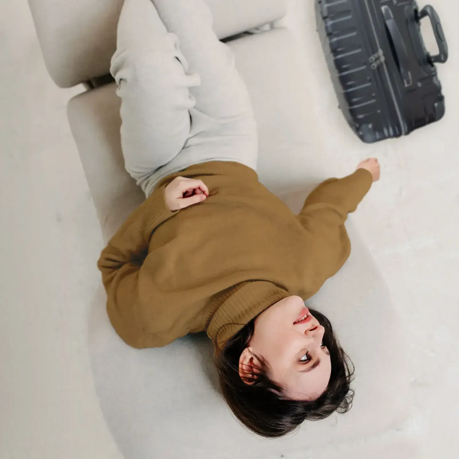 Eine Frau liegt entspannt auf einem hellen Sofa und blickt nach oben.