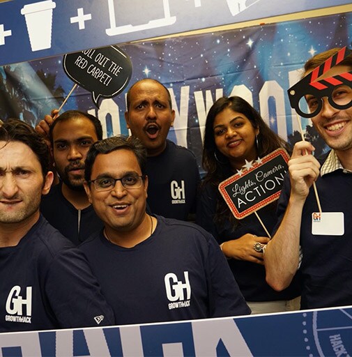 Sechs Kollegen bei einer Veranstaltung posieren in einem Kartonrahmen, auf dem „GrowthHack“ steht