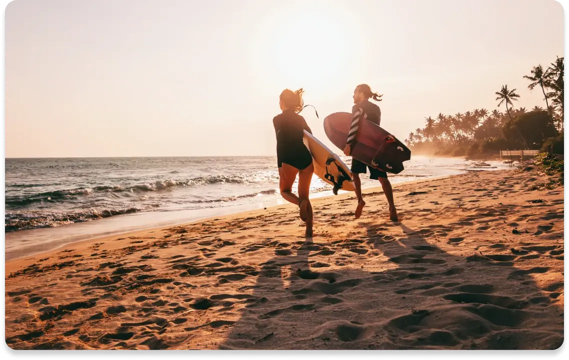 Zwei Personen laufen mit Surfboards am Strand entlang