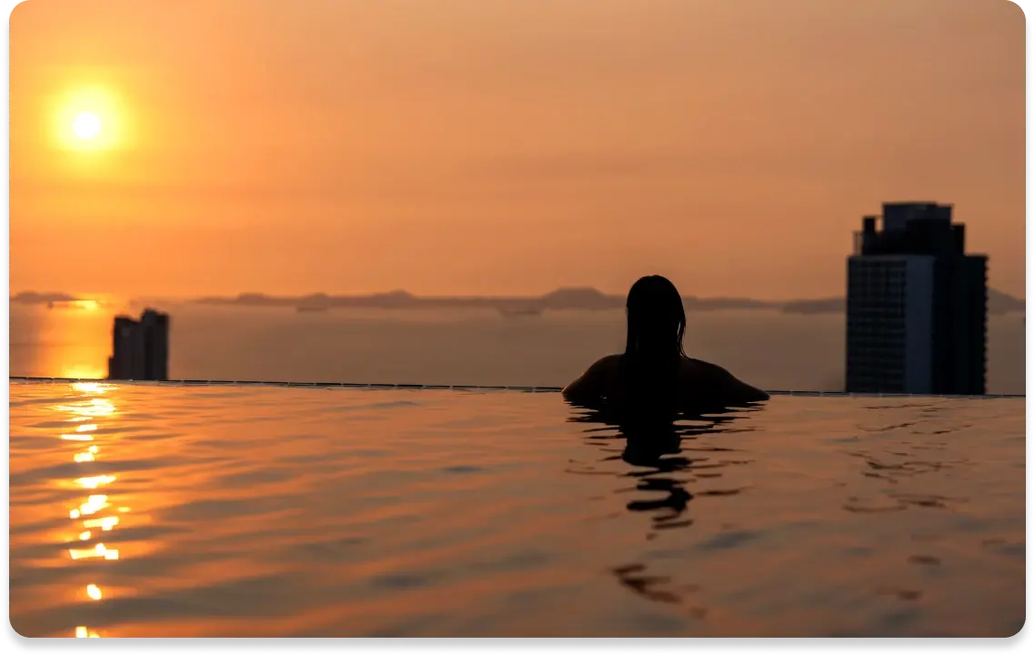 Person sitzt in einem Infinity Pool mit Blick auf Sonnenuntergang