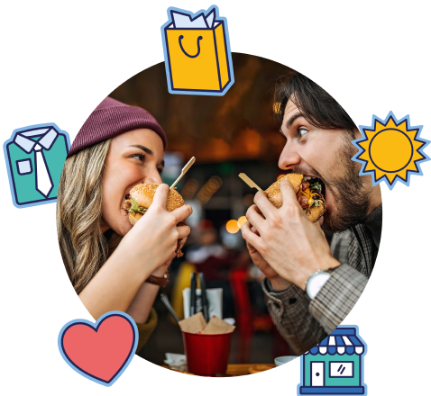 Frau und Mann sitzen sich in einem Restaurant gegenüber und beißen gleichzeitig in ihre Burger, während sie sich lachend anschauen.