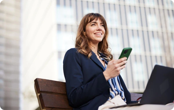 Amex App - Frau sitzt entspannt mit Smartphone und Laptop auf einem Sessel im Businessbereich.